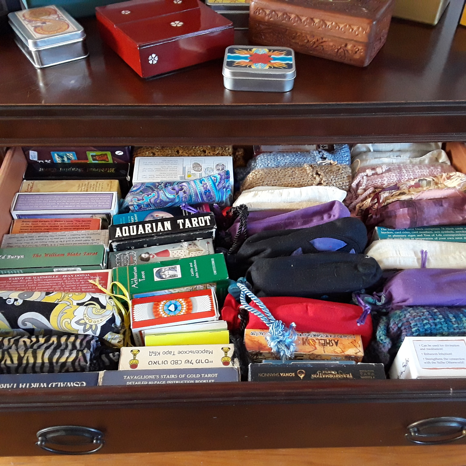 Examples of tarot storage including tuckboxes, sturdy commercial cardboard boxes, cotton drawstring tarot bags, handknit drawstring tarot bags, inexpensive muslin bags, hand-crocheted bag, organza bag, etc.