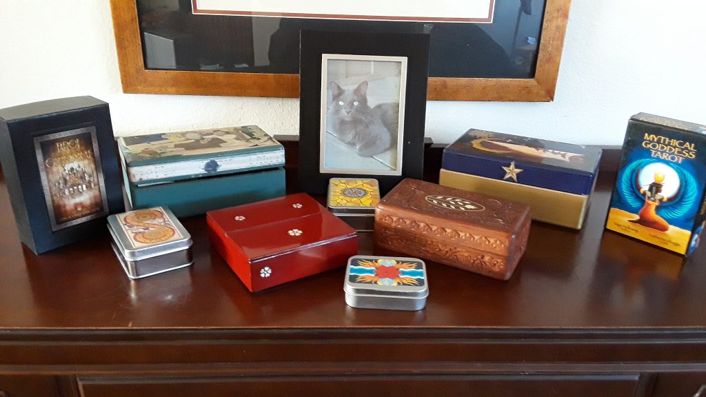 Examples of boxes for tarot storage: decoupaged wood, carved wood, sturdy commercial cardboard boxes, enameled box, and tins.